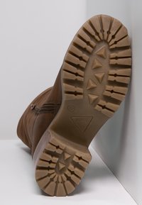 Botte en cuir marron avec une semelle texturée dotée de crampons triangulaires, fermeture éclair latérale et col légèrement rembourré. Taille indiquée comme 37.