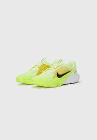 Bežecké topánky Nike s jasne žltým zvrškom, čiernym logom swoosh a bielou medzipodrážkou. Obsahujú textúrovaný vzor a šnúrky pre bezpečné uchytenie.
