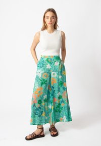 Bloemrijke wijde broek in het groen, gekenmerkt door verschillende kleurrijke bloemen. Zachte stof met zijzakken en een relaxed fit. Draagt bij een geribbelde witte top.