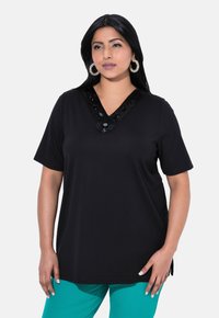 Camiseta negra de cuello en V con mangas cortas, que presenta detalles de lentejuelas en el escote, combinada con pantalones en color verde azulado. Textura suave, corte relajado.
