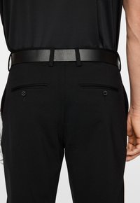 Svarta byxor med bälte som har bakfickor med knappstängning. Materialet verkar slätt, med en figursydd design och rena linjer.