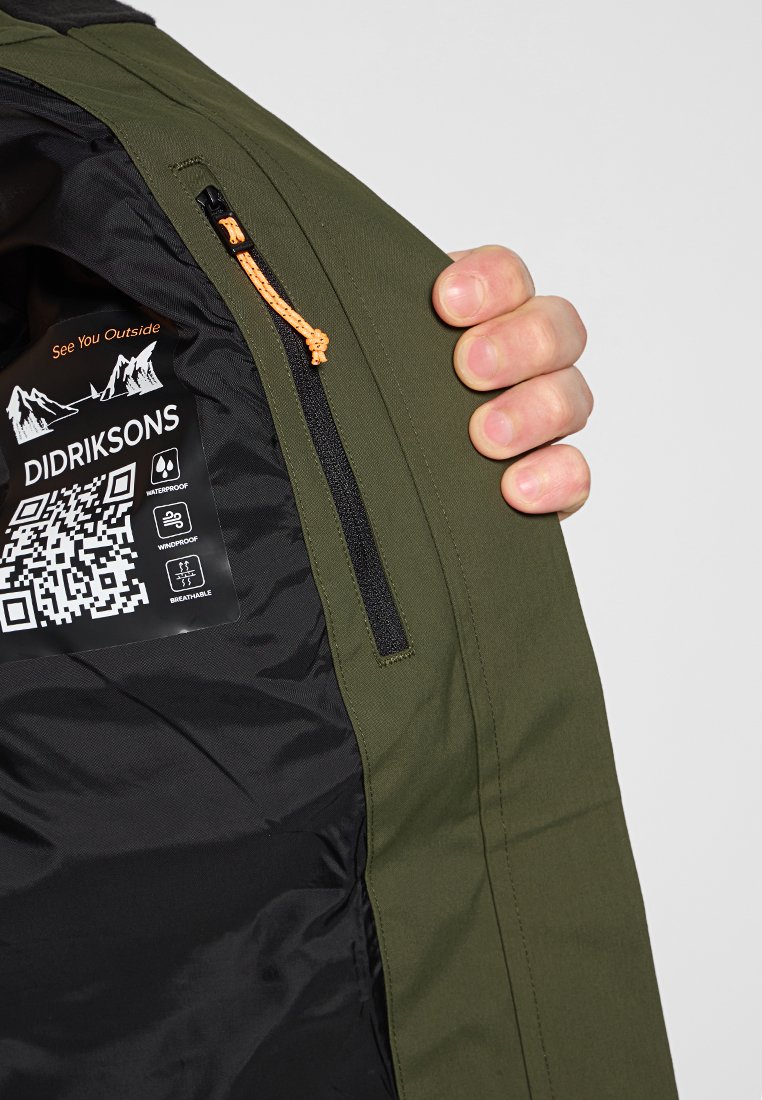Grüne wasserdichte Jacke innen, mit schwarzem Futter, Reißverschlusstasche mit orangefarbener Zuglasche und einem Etikett mit Pflegeanweisungen und QR-Code.