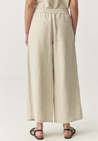 Beige linnen wijde broek met een elastische tailleband, twee achterzakken en een losse pasvorm. Lichtgewicht textuur, geschikt voor warm weer.