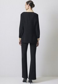 Zwart op maat gemaakt outfit met een langemouwen top met een crèmekleurige kraag en bijpassende flared broeken, aangevuld met hoge schoenen.