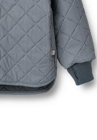 Blå quiltet ærme på jakke med diagonalt stribet mønster, ribbet manchet, buet kant og lille beige stofmærke i sidesøm.