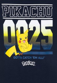 Tamno plava majica s grafikom Pikachu, s detaljima u žutoj i crnoj boji, "PIKACHU 0025" i tekstom "Gotta Catch 'Em All!".
