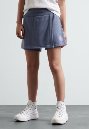 Jupe-culotte en mélange de coton bleu avec une taille ajustée, des coutures latérales et un détail de logo circulaire en rose, assortie à des baskets montantes blanches.