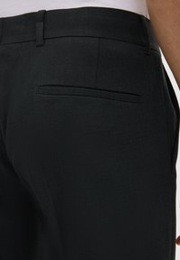 Zwarte broek met textuur, voorzien van een tailleband en een enkele achterzak. De stof heeft een subtiel geweven patroon en een elegante uitstraling.