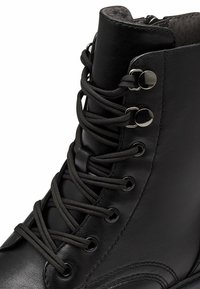 Bota de cuero negro con caña alta, punta redonda y diseño de cordones. Ojetes metálicos prominentes y forro interior texturizado.