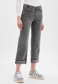 Jean en denim gris avec une coupe courte et des jambes larges. Présente un ourlet roulé et de grandes poches arrière. Associé à des baskets grises.