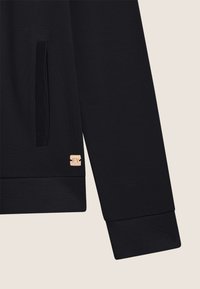 Tessuto di felpa nero con una texture liscia, caratterizzato da un polsino a coste e un piccolo logo quadrato in oro rosa sull'orlo.