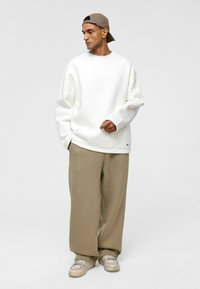 Witte oversized sweatshirt van zachte stof, gecombineerd met losse beige broeken en gedragen met lichtgekleurde sneakers en een beige pet.