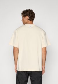 Lys beige t-skjorte med korte ermer laget av bomull, med en avslappet passform, rund hals, og en liten logoetikett på baksiden av halsen.