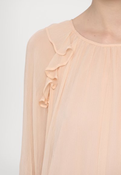 Peachfarvet bluse med en blød, gennemsigtig tekstur, der har flæsedetaljer langs halsudskæringen og en afslappet pasform.