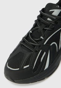 Pantofii sport negri cu un superior din plasă, accente albe contrastante și talpă din cauciuc texturat. Prezintă sistem de șireturi tradițional și un design căptușit.