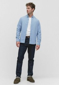 Lichtblauw overhemd met knopen, wit T-shirt eronder, donkerblauwe spijkerbroek en bruine schoenen. Eenvoudig ontwerp met lange mouwen en manchetten.