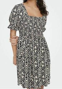 Robe à motif noir et crème, avec un décolleté carré, de courtes manches bouffantes, et une taille smockée avec une jupe fluide.