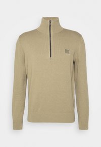 Světlé béžové svetr s vysokým límcem, polovičním zipem vpředu, žebrovanými manžetami a spodním lemem. Na hrudi je čtvercová logo nášivka.