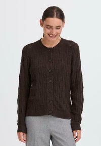 Ruske knit vest med kabelmønster, rund hals og knappestolpe. Har ribbemansjetter og -kant, middels tykkelse og lange ermer.