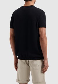 Zwart kortomslagantrui van een gestructureerde, lussenstof. Geribbelde kraag en zoom. Combineert met beige shorts, wat een casual look laat zien.