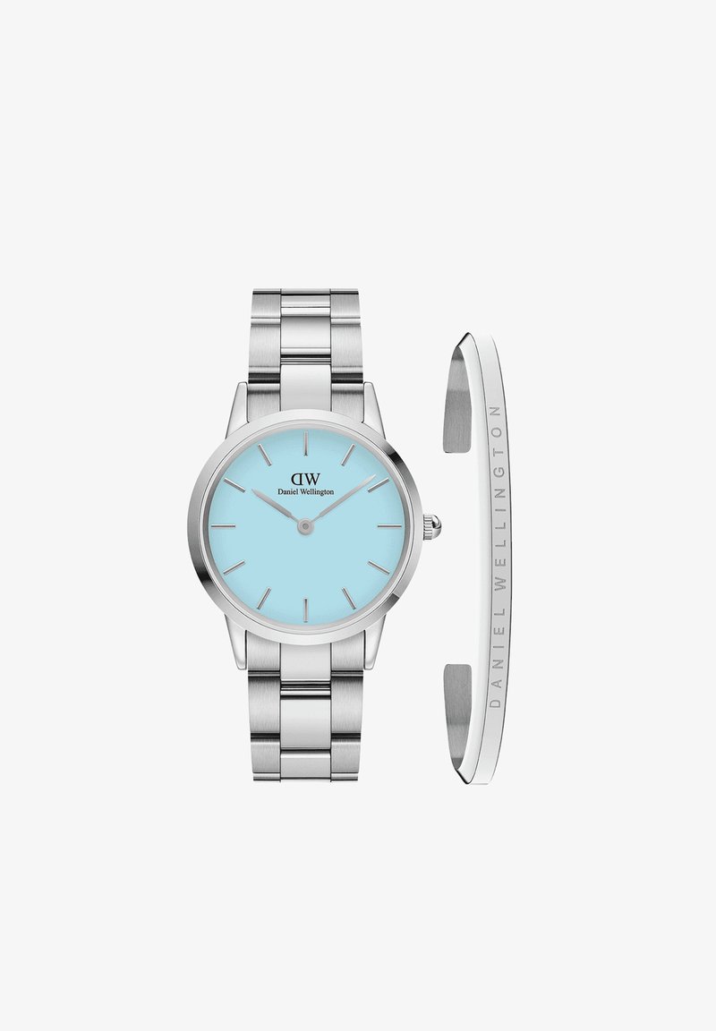 Hõbe metallkell ümmarguse korpusega, helesinise kellakuvandi, hõbedaste käte ja tunnusmarkidega. Komplektis on hõbedane käevõru ja logoga mansett.