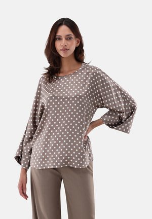 Top beige a pois in un tessuto morbido con una vestibilità ampia, maniche larghe e scollo rotondo, abbinato a pantaloni beige chiaro.