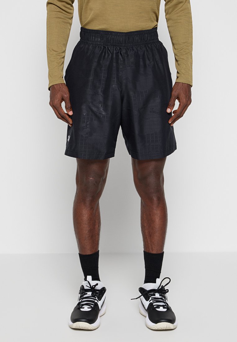 Schwarze Sportshorts mit einem elastischen Bund, die ein quadratisches Muster und ein kleines Logo am linken Saum aufweisen. Kombiniert mit schwarz-weißen Turnschuhen.