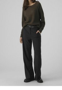 Maglione in maglia testurizzata verde oliva con scollatura ampia, abbinato a pantaloni neri a gamba larga con tasche frontali e cintura. Scarpe nere.