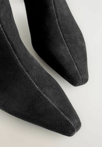 Chaussures à talons hauts en daim noir avec une pointe fine et une texture lisse. Les coutures latérales sont visibles, mettant en valeur le design élégant de la chaussure.