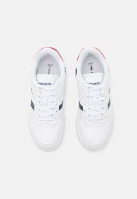 Hvit sneaker med en glatt skinnoverdel, marineblå og røde detaljer, snøring og perforerte detaljer på tådelen. Logo på tungen.