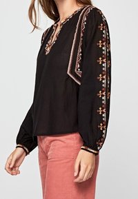 Black blouse with long sleeves, featuring colorful embroidered patterns along the shoulders and cuffs, and a small V-neck opening.