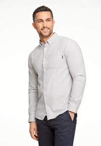 Lichtgrijs, lange mouwen knoopoverhemd van stof met een zachte textuur. Bevat een enkele borstzak en witte knopen. Gemaakt met donkere broek.