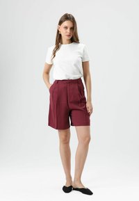 Wit T-shirt met korte mouwen gecombineerd met hoge taille, bordeauxrode shorts. Glad materiaal met een losse pasvorm, aangevuld met zwarte instapschoenen.