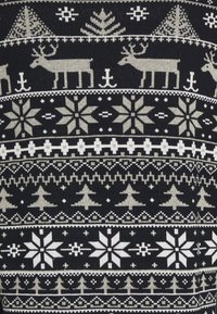 Pletený svetr s tmavě modrým pozadím a bílými a béžovými geometrickými vzory, včetně jelenů, stromů a sněhových vloček.