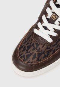 Brun sneaker med et mønstret tekstiloverdel med et brunligt grafisk design, hvide snørebånd og en glat brun læderkant. Hvid gummisål.