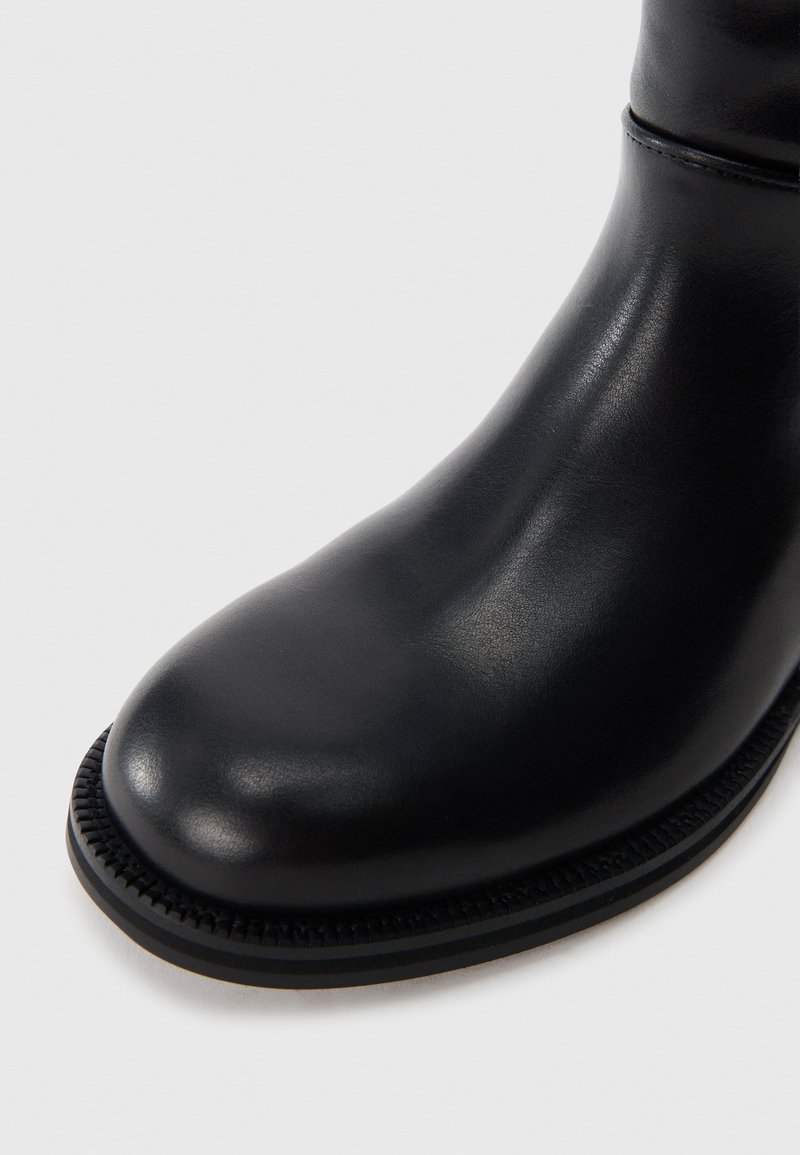 Botte en cuir noir à la cheville avec un bout rond, texture lisse et détail de semelle cousue. Design minimaliste sans matériel visible.