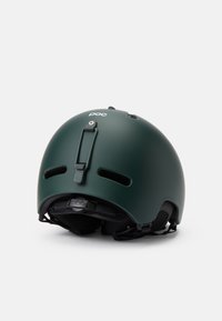Vihreä mattapintainen kypärä, jossa on säädettävä vyöjärjestelmä, ilmanvaihtoaukot ja takaklipsi. Logo näkyvissä edessä. Pyöreä muotoilu turvallisuuden vuoksi.