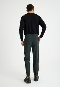 Zwarte lange mouw top gecombineerd met grijze geruite broek. De broek heeft een slim fit en zijzakken, aangevuld met zwarte sneakers.