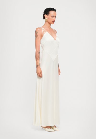 Robe longue couleur crème avec un décolleté en V, des bretelles fines et un corsage à motif en damier. Texture lisse et silhouette fluide. Design élégant.