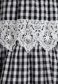 Schwarz-weiß kariertes Stoffmuster mit einem weißen Spitzenbesatz aus Blumenmuster, verziert mit kunstvollen Mustern und gewellten Kanten.