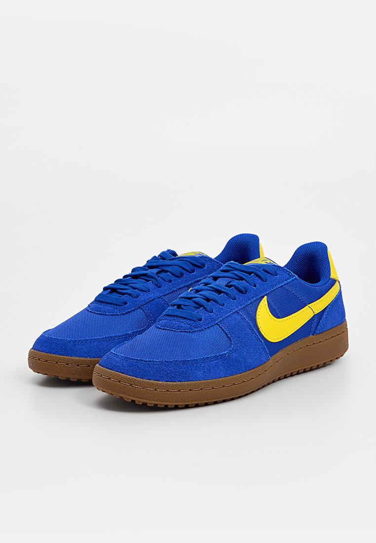 Blaue Sneakers mit einem strukturierten Stoff-Obermaterial, ausgestattet mit einem gelben Nike-Swoosh und einer braunen Gummisohle. Schnürdesign mit gepolsterter Schuhkragen.