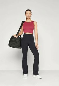 Bordový crop top, černé legíny s vysokým pasem a bílé tenisky. Nese texturovanou černou sportovní tašku. Jednoduchý, přiléhavý design.