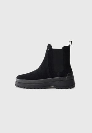 Botins pretos de camurça até ao tornozelo com painéis laterais elásticos, uma alça de puxar e uma sola de borracha texturizada, apresentando um design elegante e minimalista.
