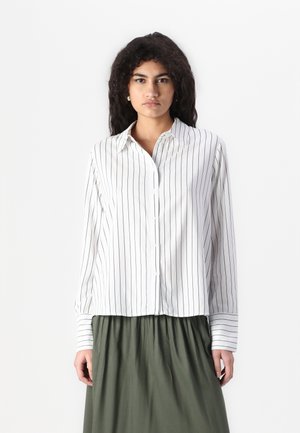 Hvit skjorte med marineblå vertikale striper, krage, lange ermer og en lett cropped hem, kombinert med et grønt skjørt.
