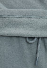Hanorac bleu deschis cu un interior din fleece moale, talie elastică și cordon cu vârf metalic. Material texturat din amestec de bumbac.