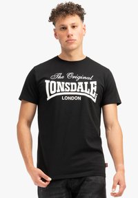 Crna pamučna majica kratkih rukava s natpisom "The Original Lonsdale London" bijele boje na prsima. Jednostavan, klasičan dizajn.