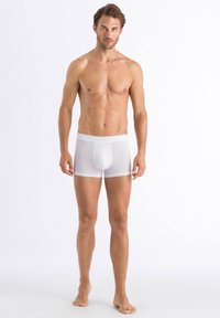 Vita boxer shorts med elastisk midja, gjorda av ett slätt, stretchy tyg. Fitted stil med en framficka. Modellen står barfota.