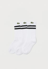 Calcetines de algodón blancos con dos rayas negras en la parte superior y un logo de cocodrilo verde. La tela tiene una textura acanalada. Se incluyen tres pares.