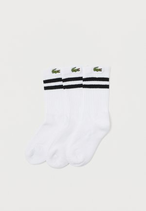 Calcetines de algodón blancos con dos rayas negras en la parte superior y un logo de cocodrilo verde. La tela tiene una textura acanalada. Se incluyen tres pares.