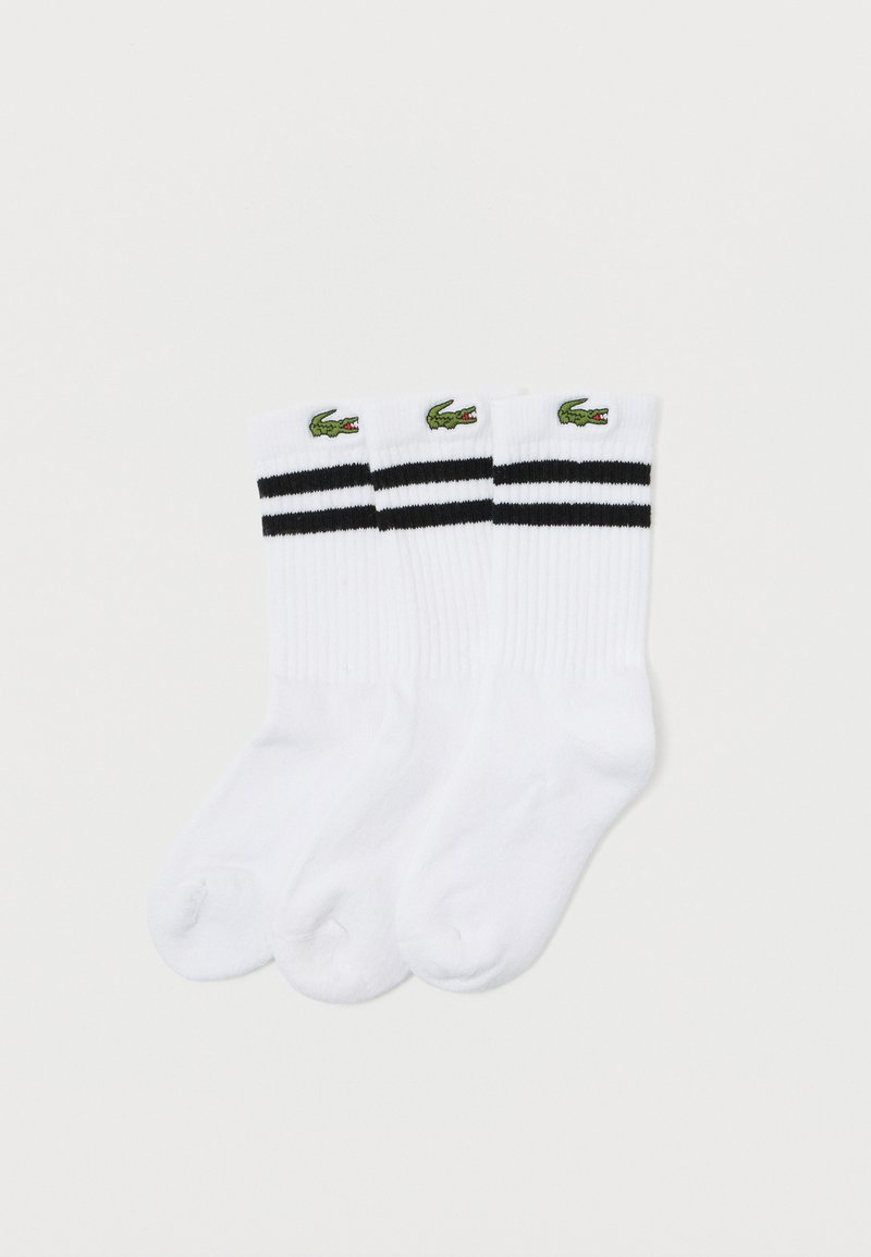 Calcetines de algodón blancos con dos rayas negras en la parte superior y un logo de cocodrilo verde. La tela tiene una textura acanalada. Se incluyen tres pares.